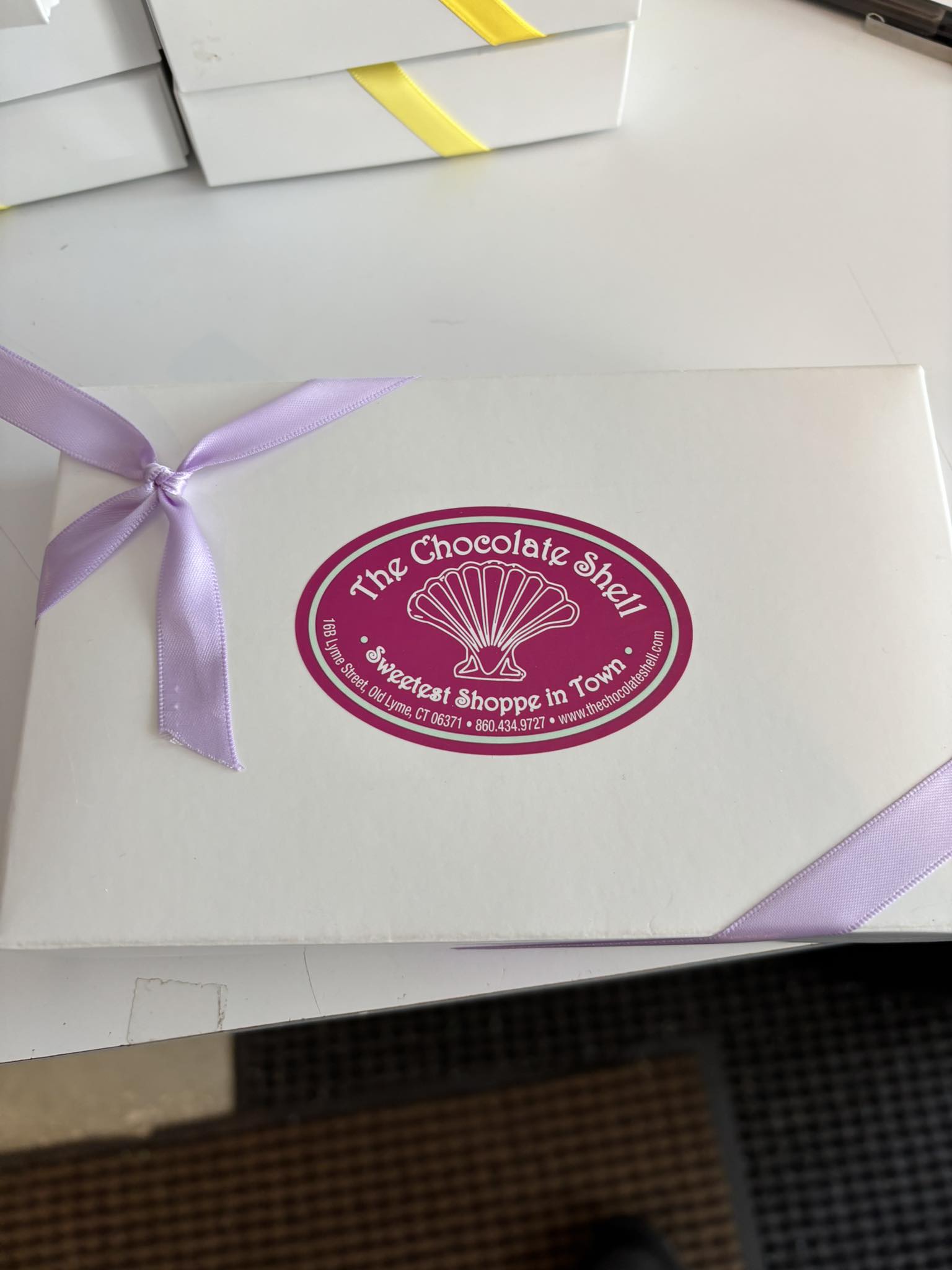 White gift box with a lavender ribbon, labeled "The Chocolate Shell,"
